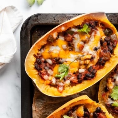 Stuffed spaghetti squash halves with beans, veggies and cheese on baking sheet.