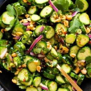 Thai cucumber salad with bread onion, peanuts and cilantro in a bowl with a spoon.