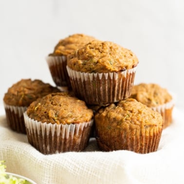 Zucchini carrot muffins stacked on top of each other and bowl with shredded zucchini near it.