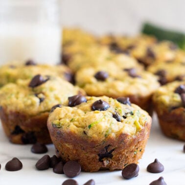 Zucchini chocolate chip muffins, glass of milk and chocolate chips on a counter.
