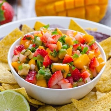 Strawberry mango salsa in white bowl on plate with chips.