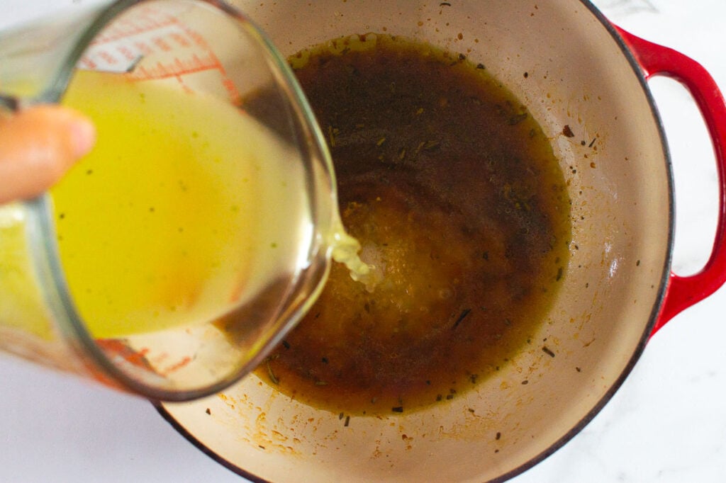 pouring chicken stock to a pot with drippings
