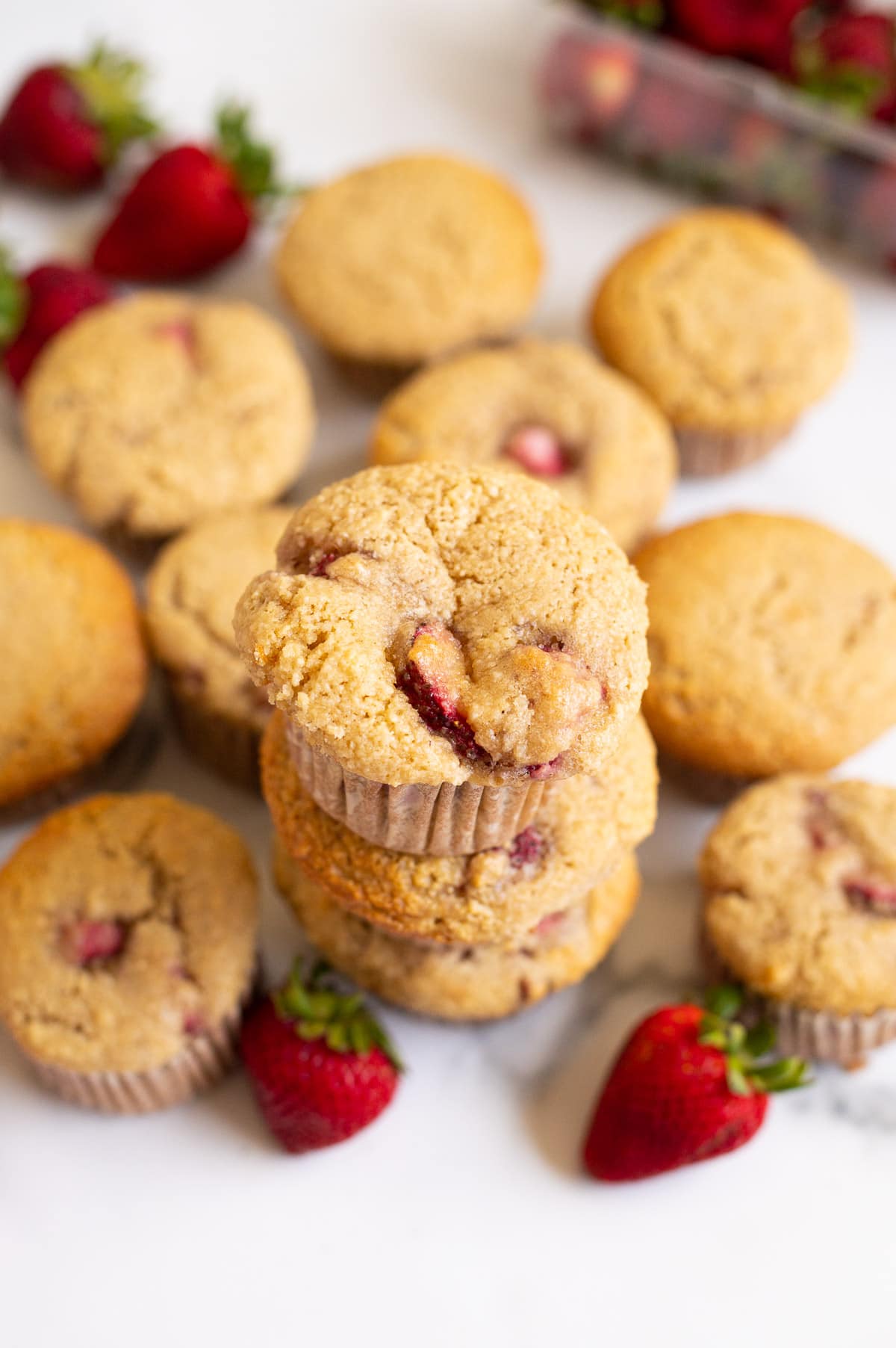 Almond flour muffins with strawberries on a countertop and fresh strawberries around them.