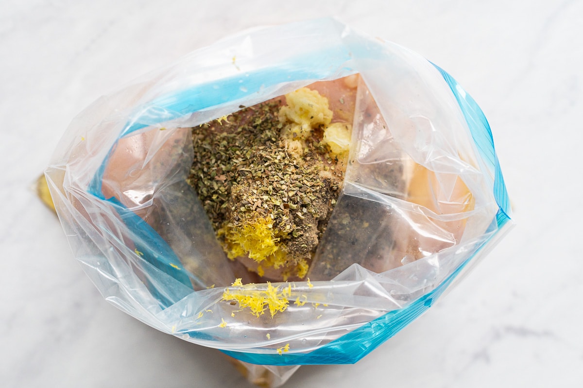 Chicken breasts marinated in oil, lemon, garlic and spices in a Ziploc bag.