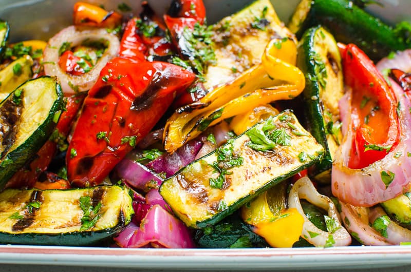 Grilled zucchini, bell peppers and red onions with balsamic vinaigrette in a baking dish.