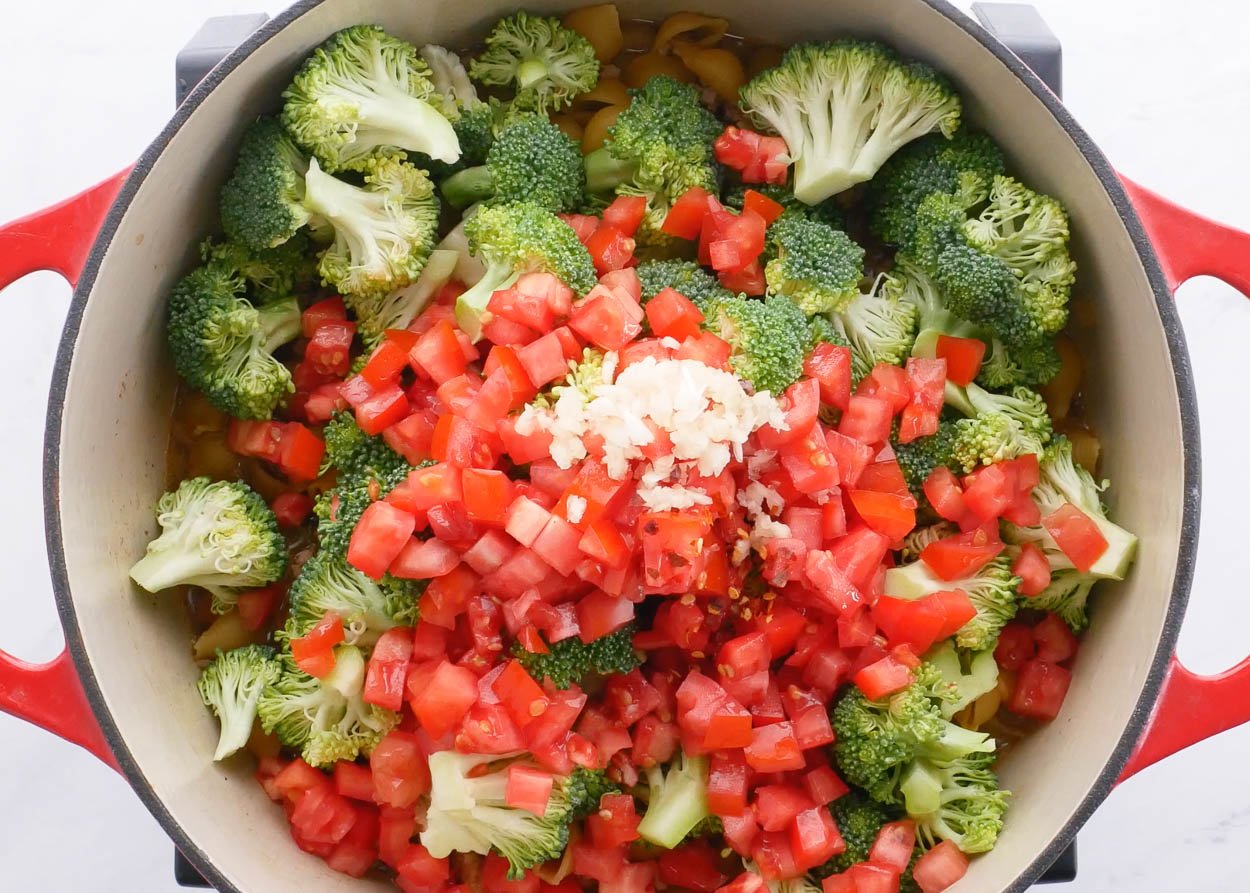 A pot with broccoli, tomatoes and garlic.