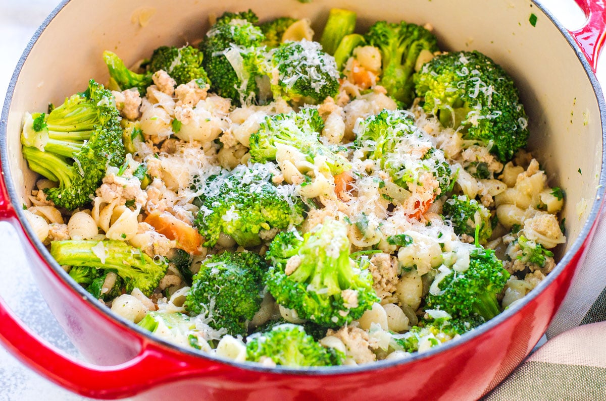 A red pot with broccoli, pasta, ground turkey and tomatoes, garnished with Parmesan.
