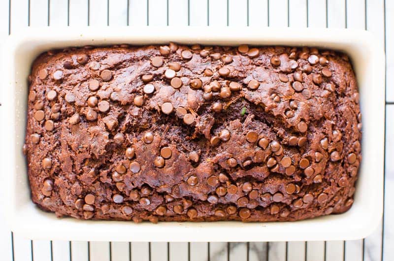 Healthy chocolate zucchini bread with mini chocolate chips in a loaf pan on a cooling rack.