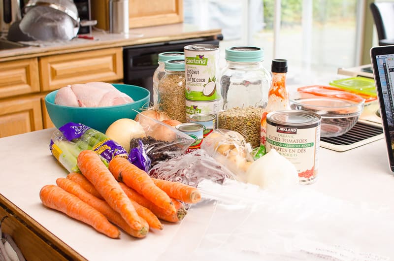 Carrots, celery, beans, chicken, potato, onion, canned goods on a counter.