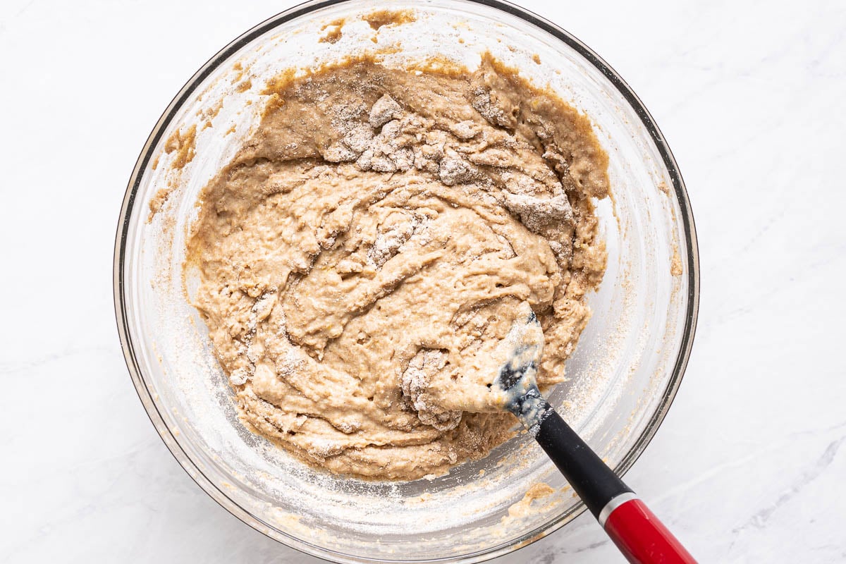 Flour being stirred into batter in a bowl with a spatula.