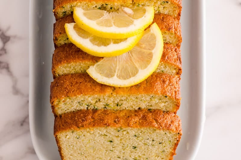 Slices of healthy lemon zucchini bread with sliced lemon on top and served on a platter.