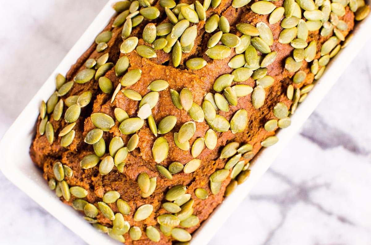 Pumpkin bread studded with pepitas in a loaf pan on a counter.