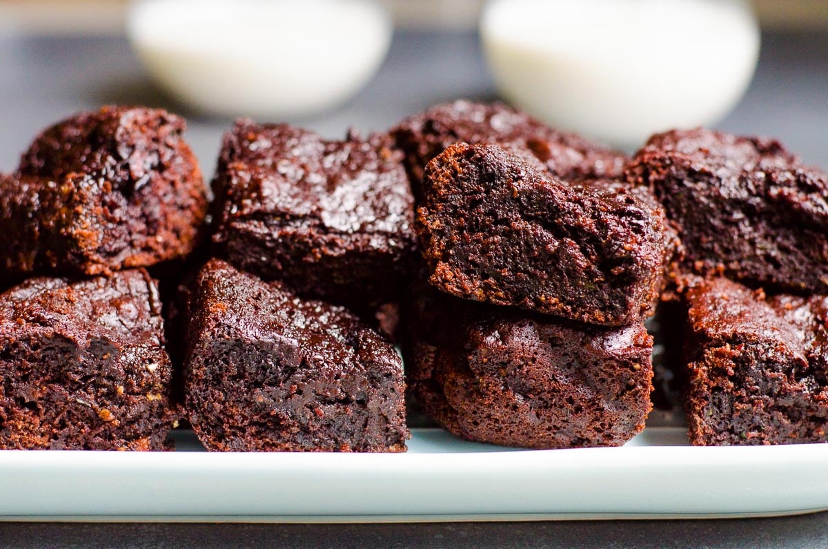 Healthy zucchini brownies on a platter with two glasses of milk in the background.