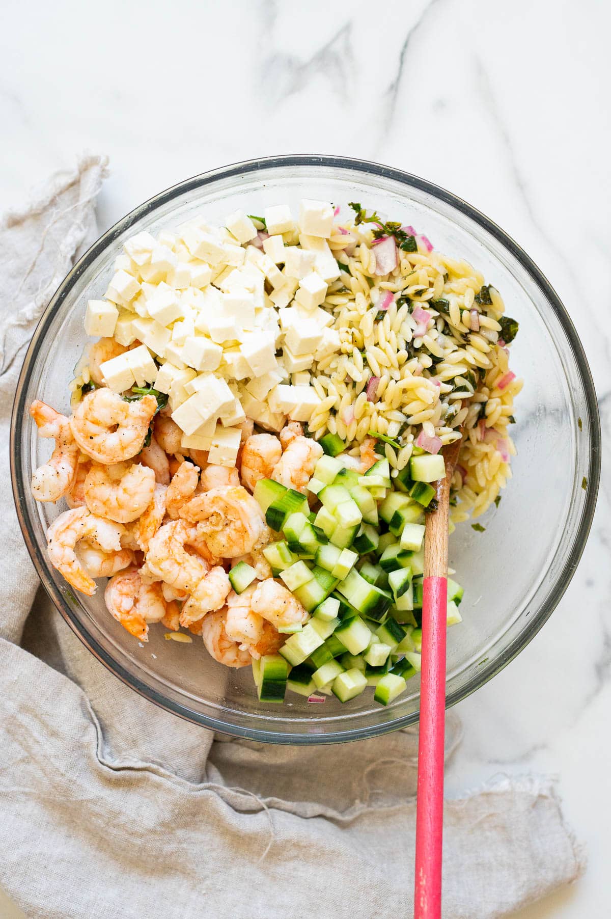 Cooked shrimp, cubed feta cheese, diced cucumber and orzo with the dressing in a bowl.