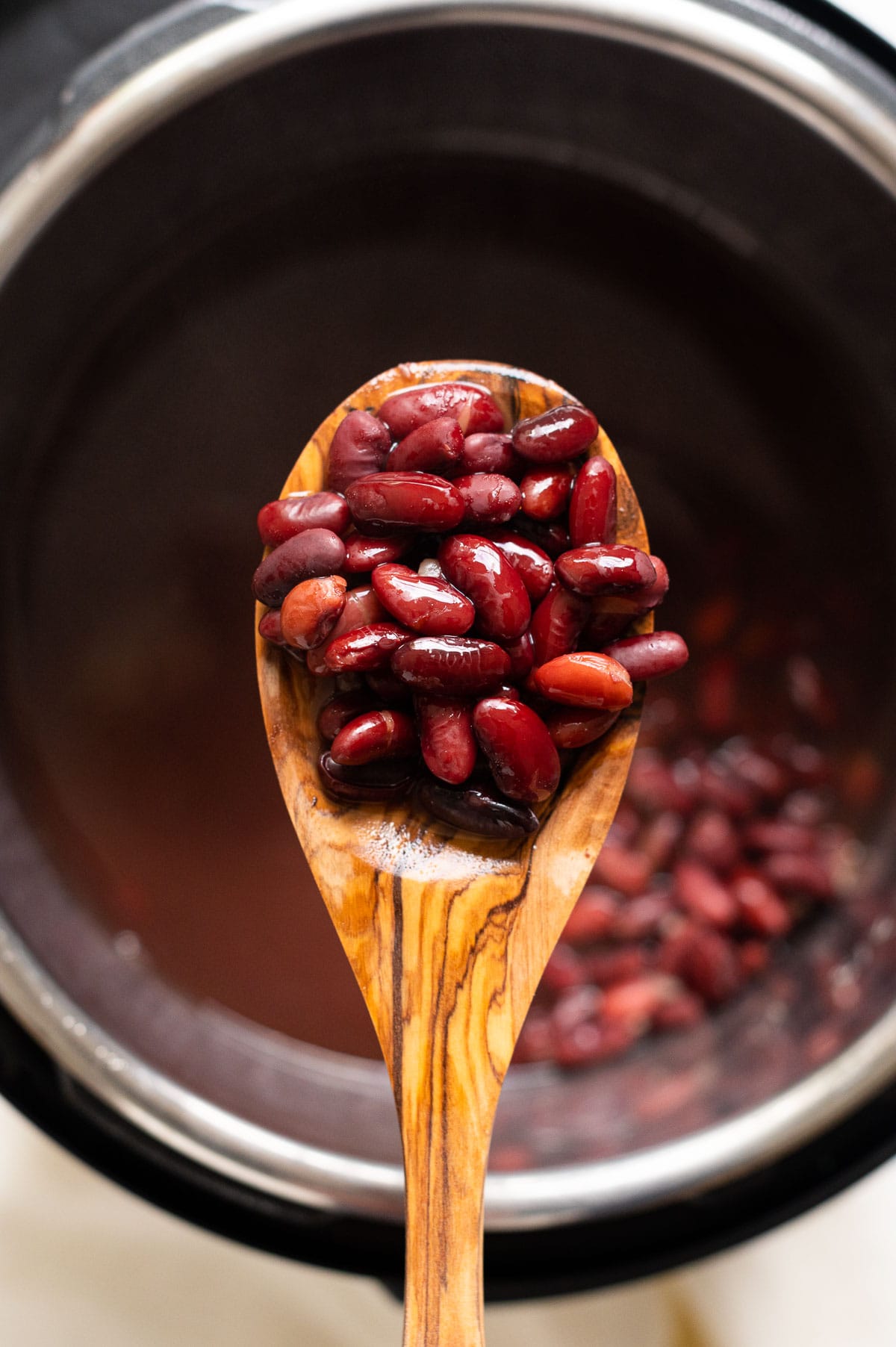 Instant pot kidney beans on a wooden spoon above the pot.