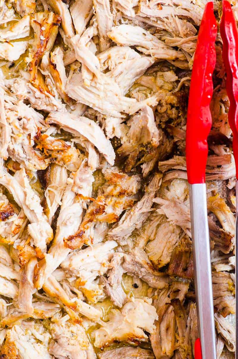 shredded Instant Pot pork carnitas with red tongs on a tray