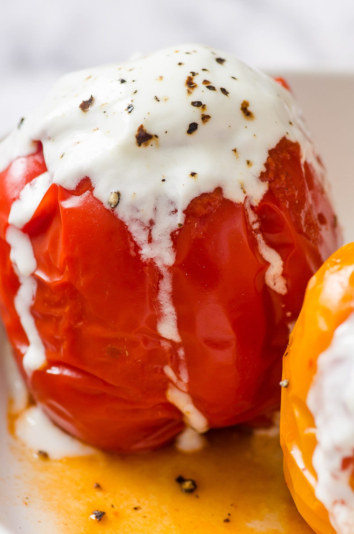 Instant pot stuffed peppers served with yogurt and ground black pepper on top with juices on a plate.