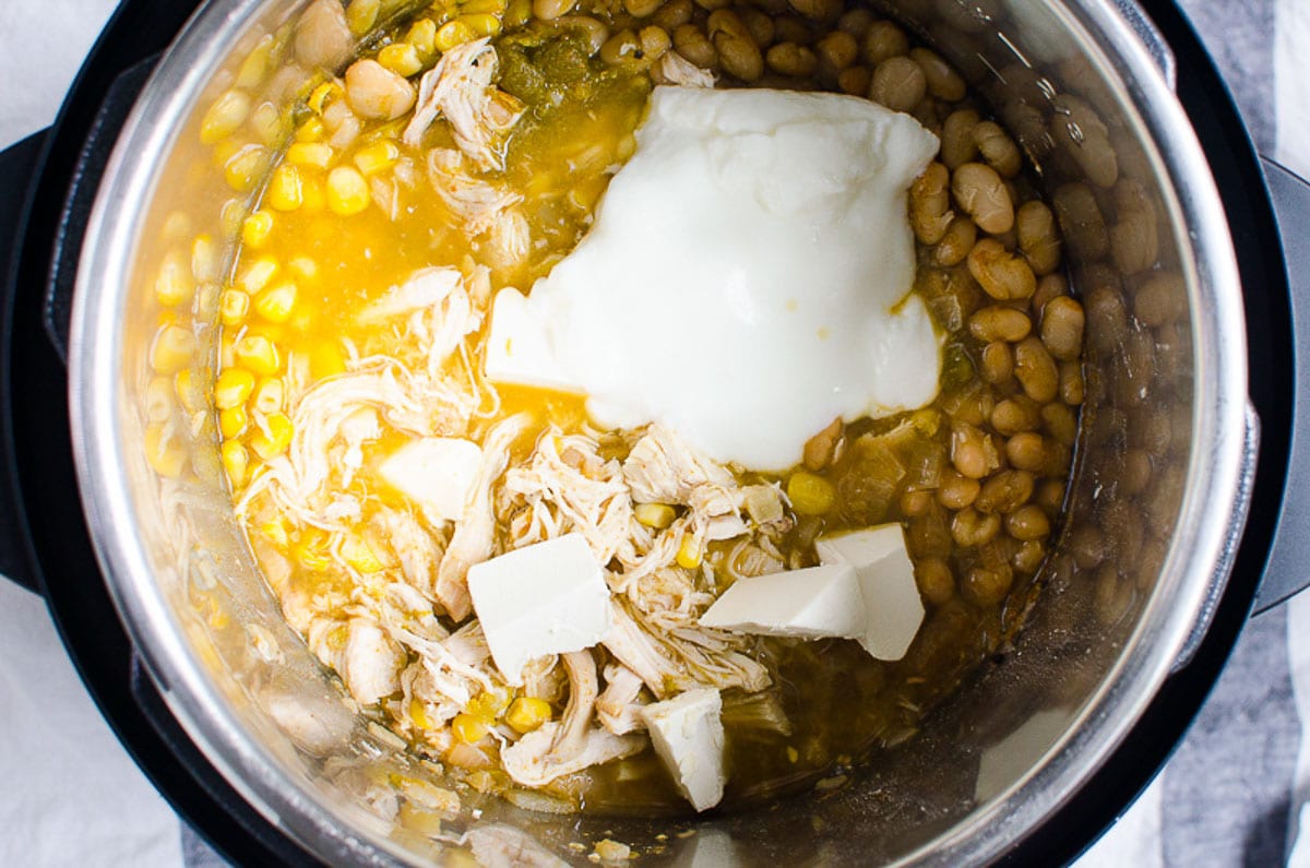 Greek yogurt and cubed cream cheese in Instant Pot with shredded chicken.