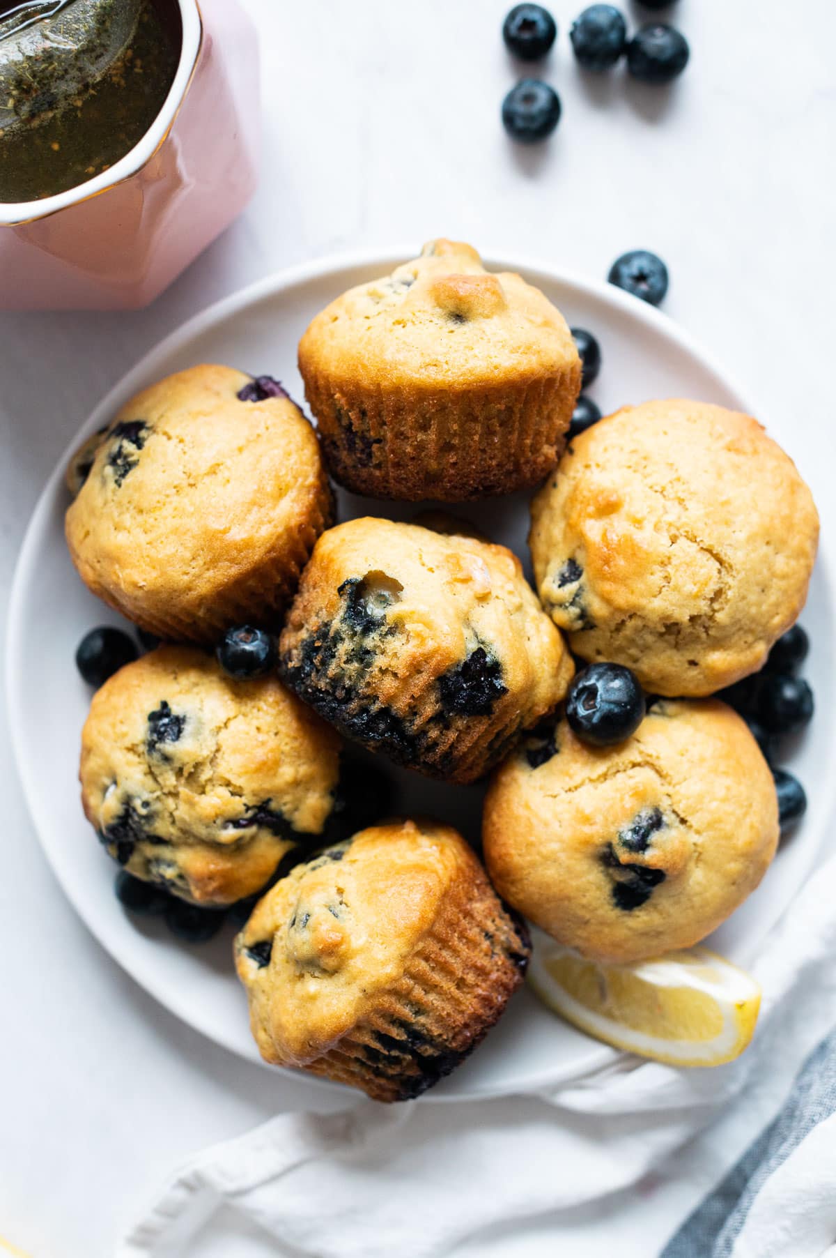 Seven lemon blueberry muffins on a plate with blueberries and lemon slice.