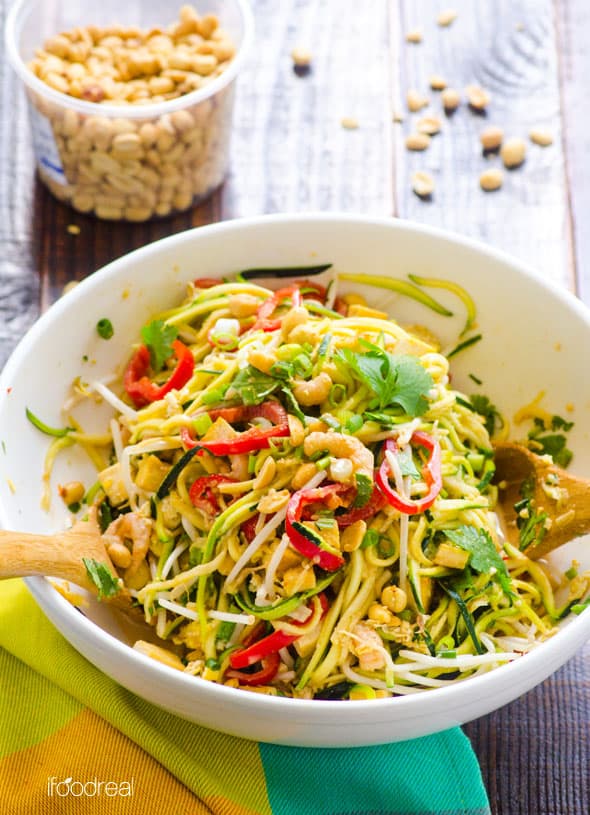 Pad Thai zucchini noodles salad served in a bowl with wooden spoons and peanuts in a container in the background.