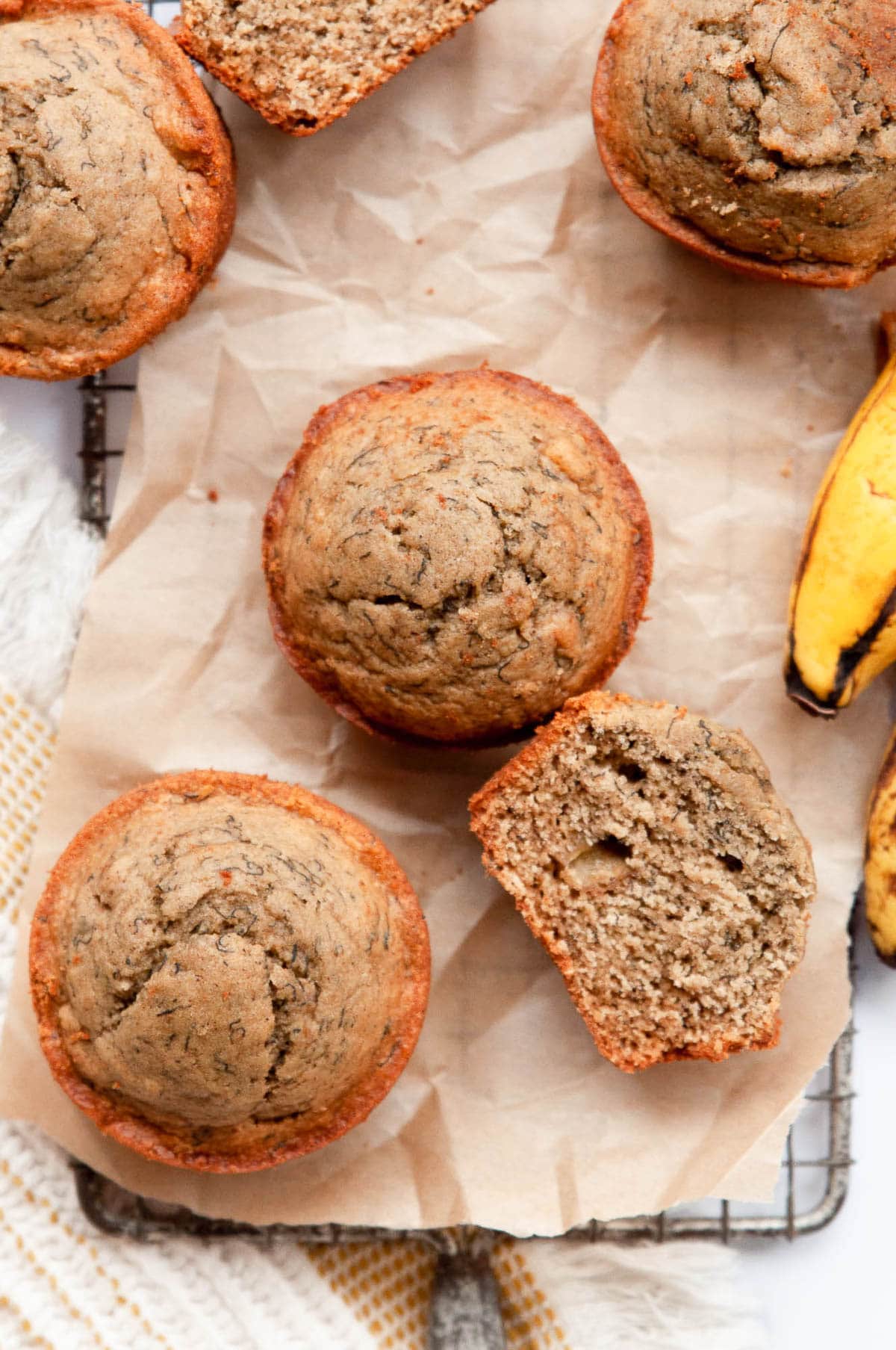 Oat flour banana muffins on parchment paper and the one muffin cut and showing texture.