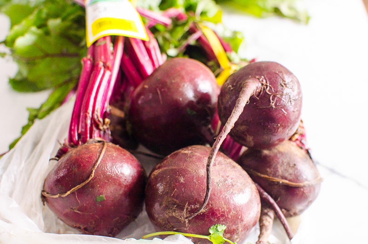 A bunch of five beets with greens on a countertop.