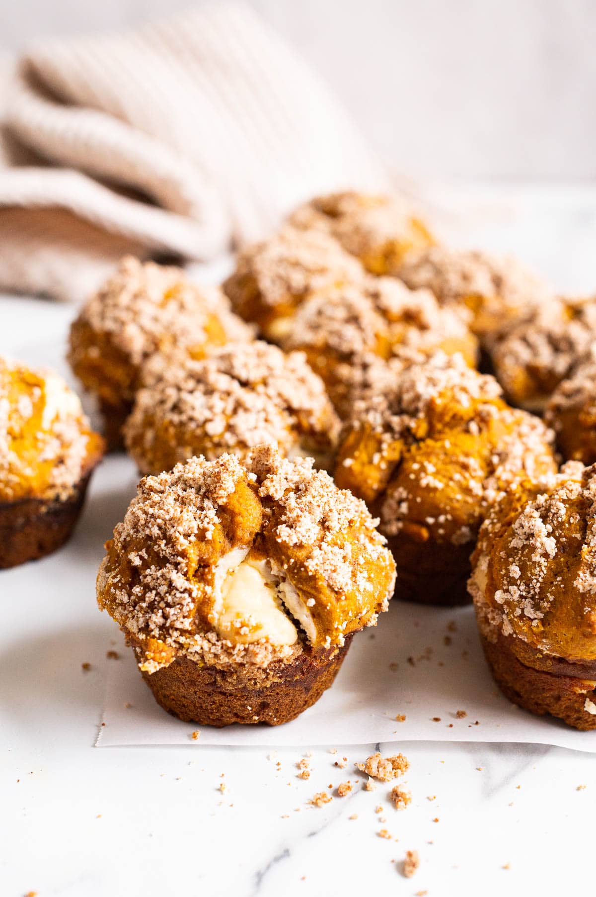 Pumpkin cream cheese muffins with streusel topping on parchment paper on a counter.