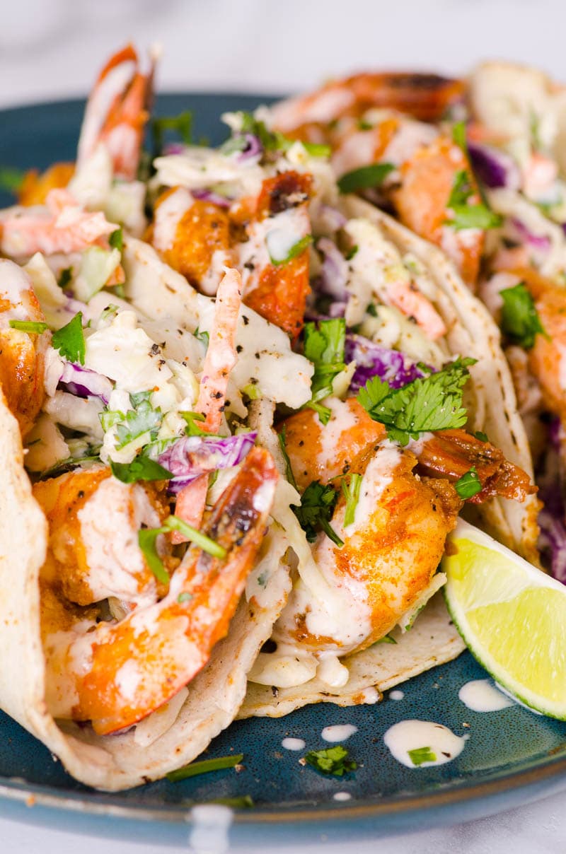Shrimp tacos with slaw and cilantro on a plate with lime wedge.