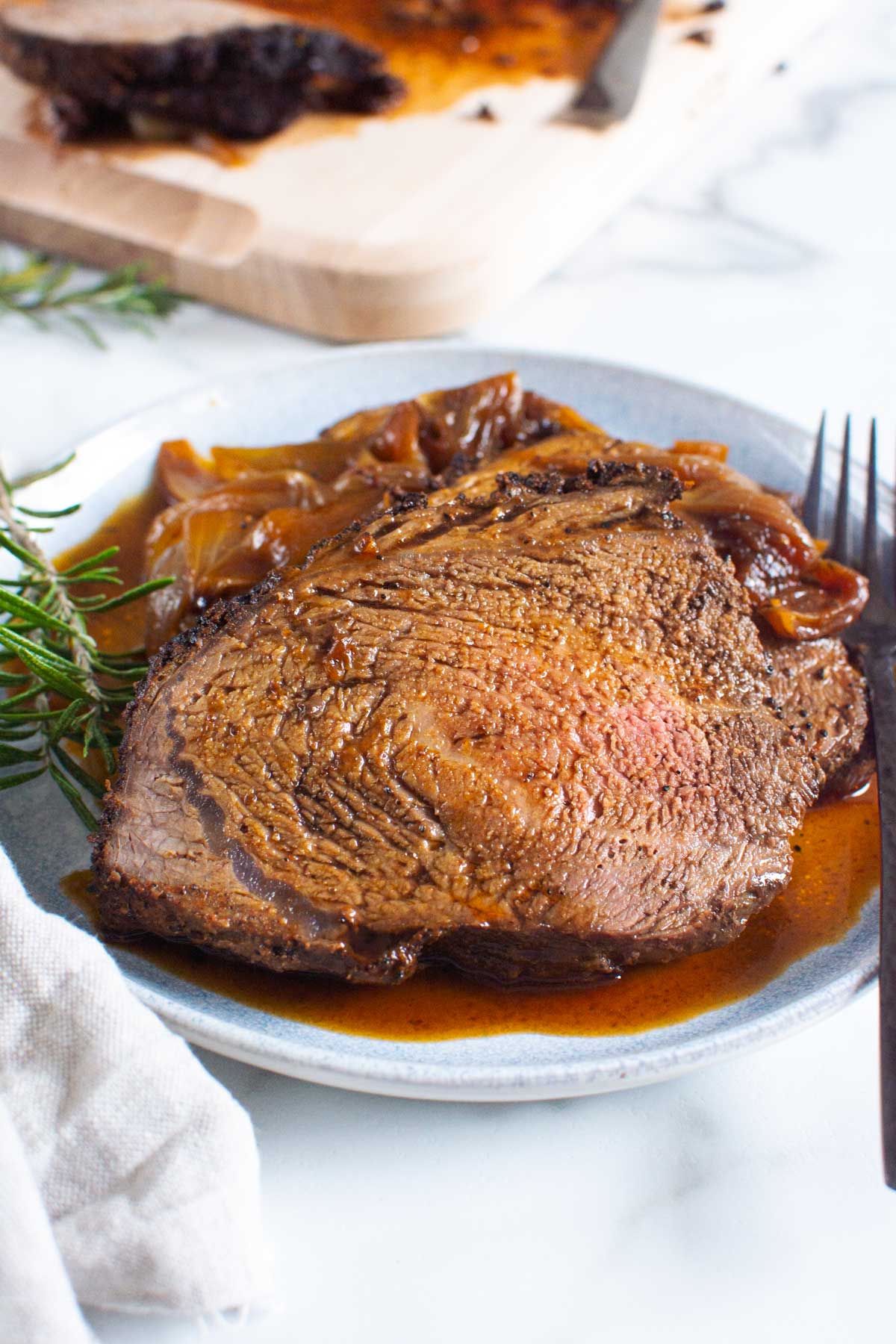Sirloin tip roast recipe with pan juices on a plate ready to eat with napkin and fork.