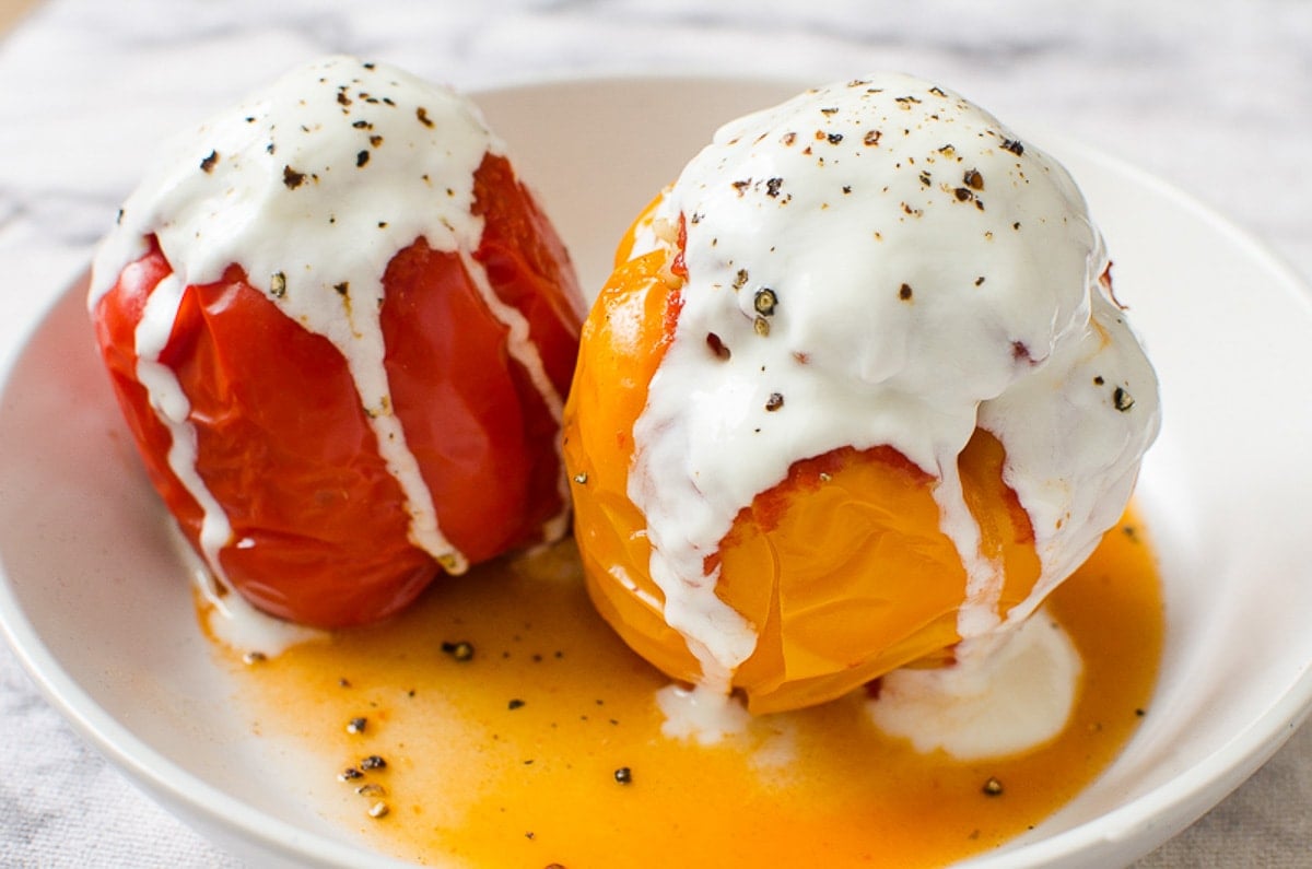 Two stuffed peppers served with their juices and yogurt on a plate.