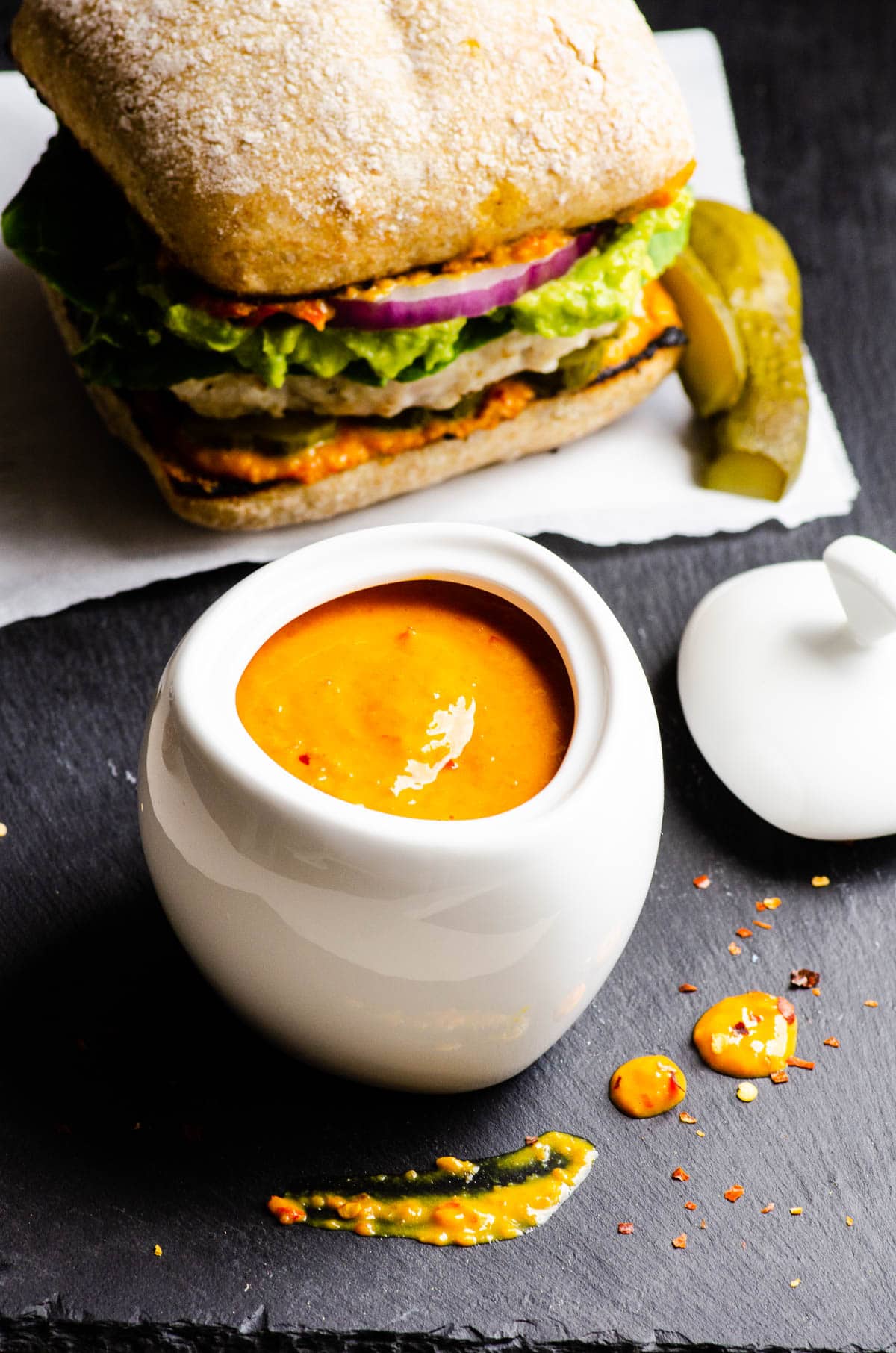 Sweet and spicy mustard in white jar. Burger and pickle on a side.
