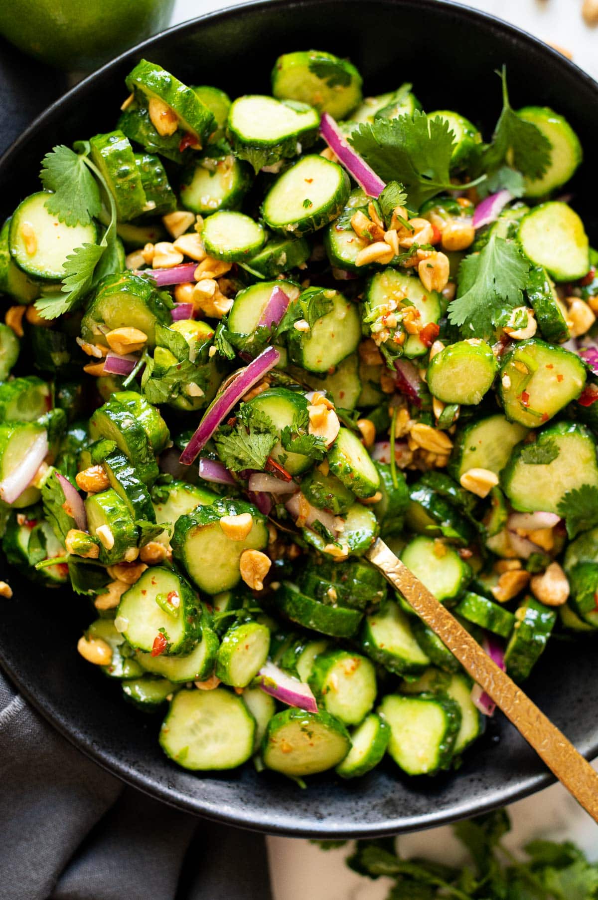 Thai cucumber salad with bread onion, peanuts and cilantro in a bowl with a spoon.