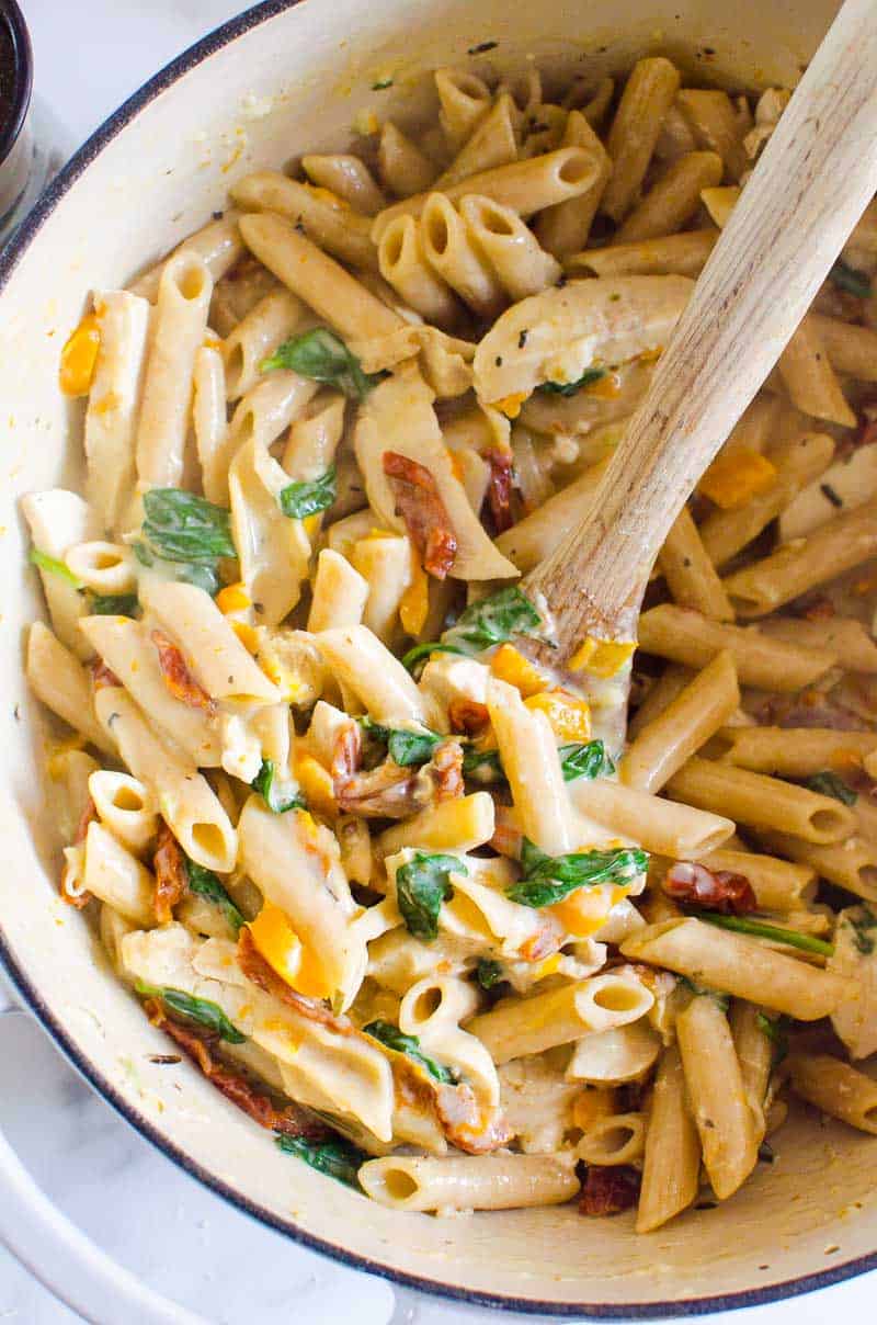 Healthy Tuscan Chicken Pasta in pot with serving spoon.