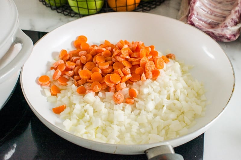Chopped onion and carrots in white skillet.