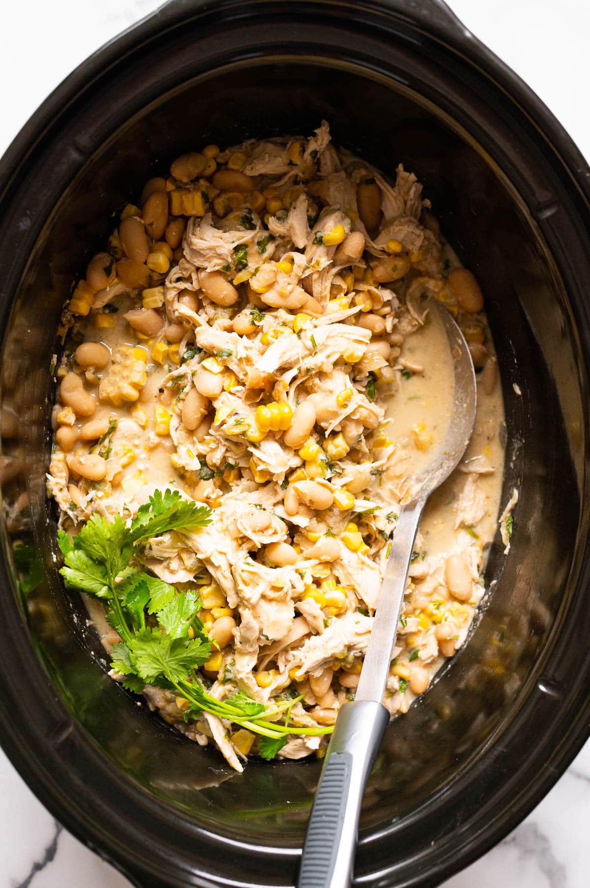 White chicken chili in slow cooker with cilantro and metal spoon.