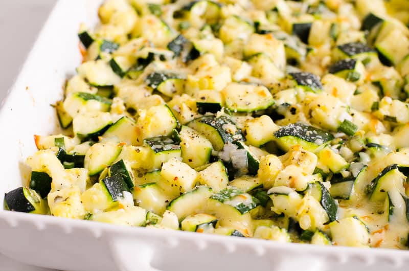 Healthy zucchini casserole with melted cheese on top in white baking dish.
