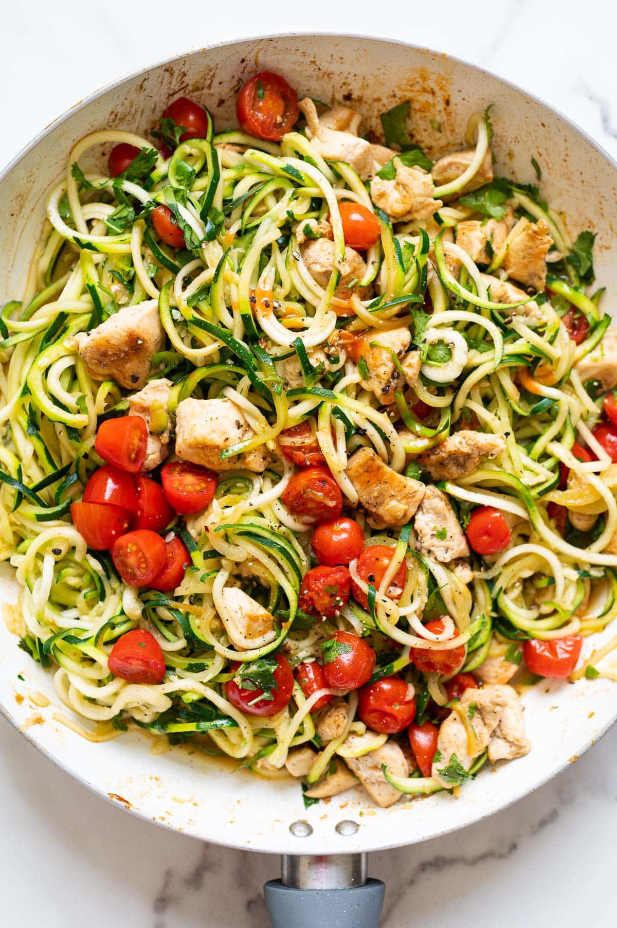 Zucchini noodles with chicken and tomatoes in a skillet.